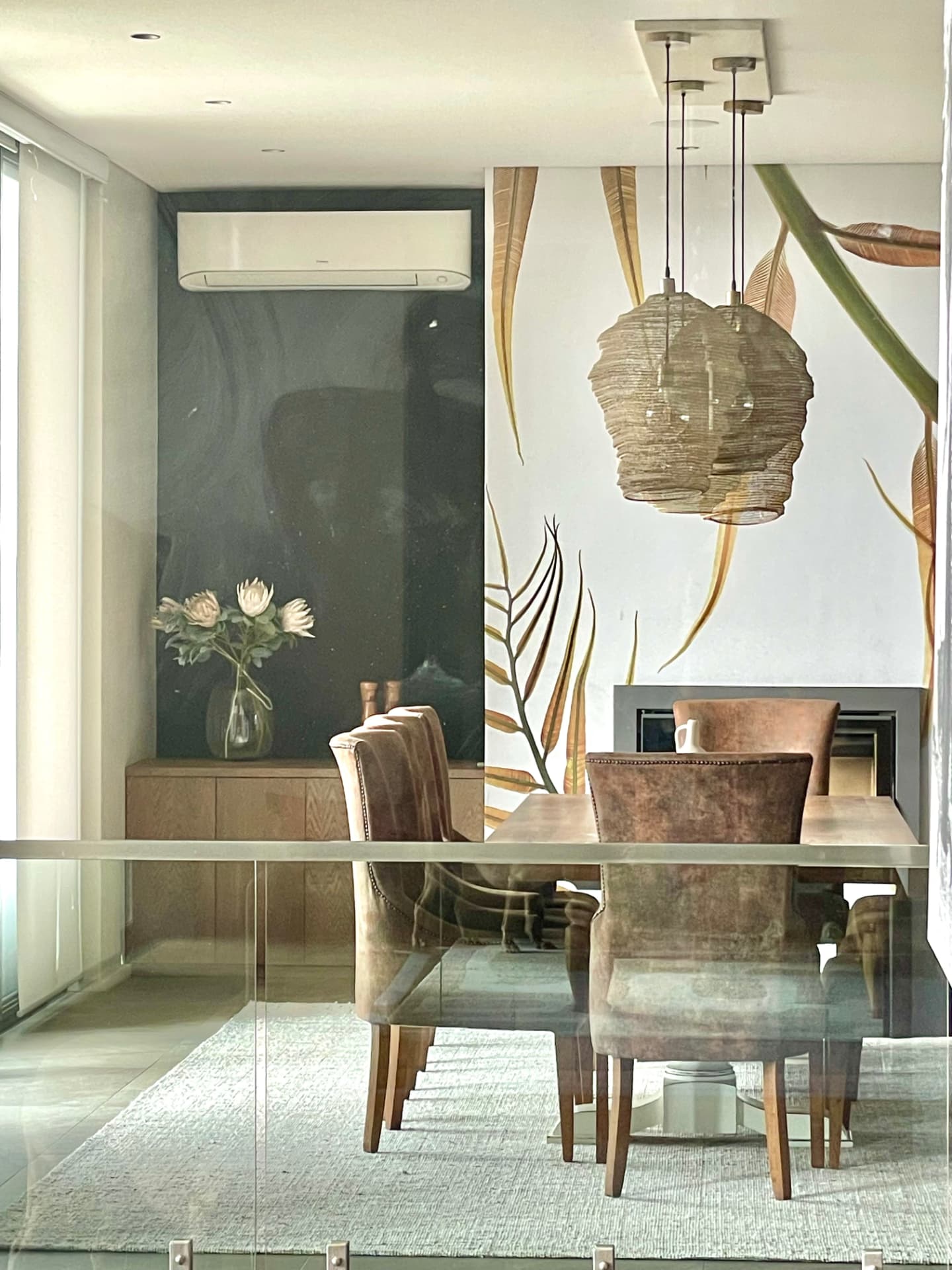 Dining space seen through glazing with protea arrangement and woven pendants
