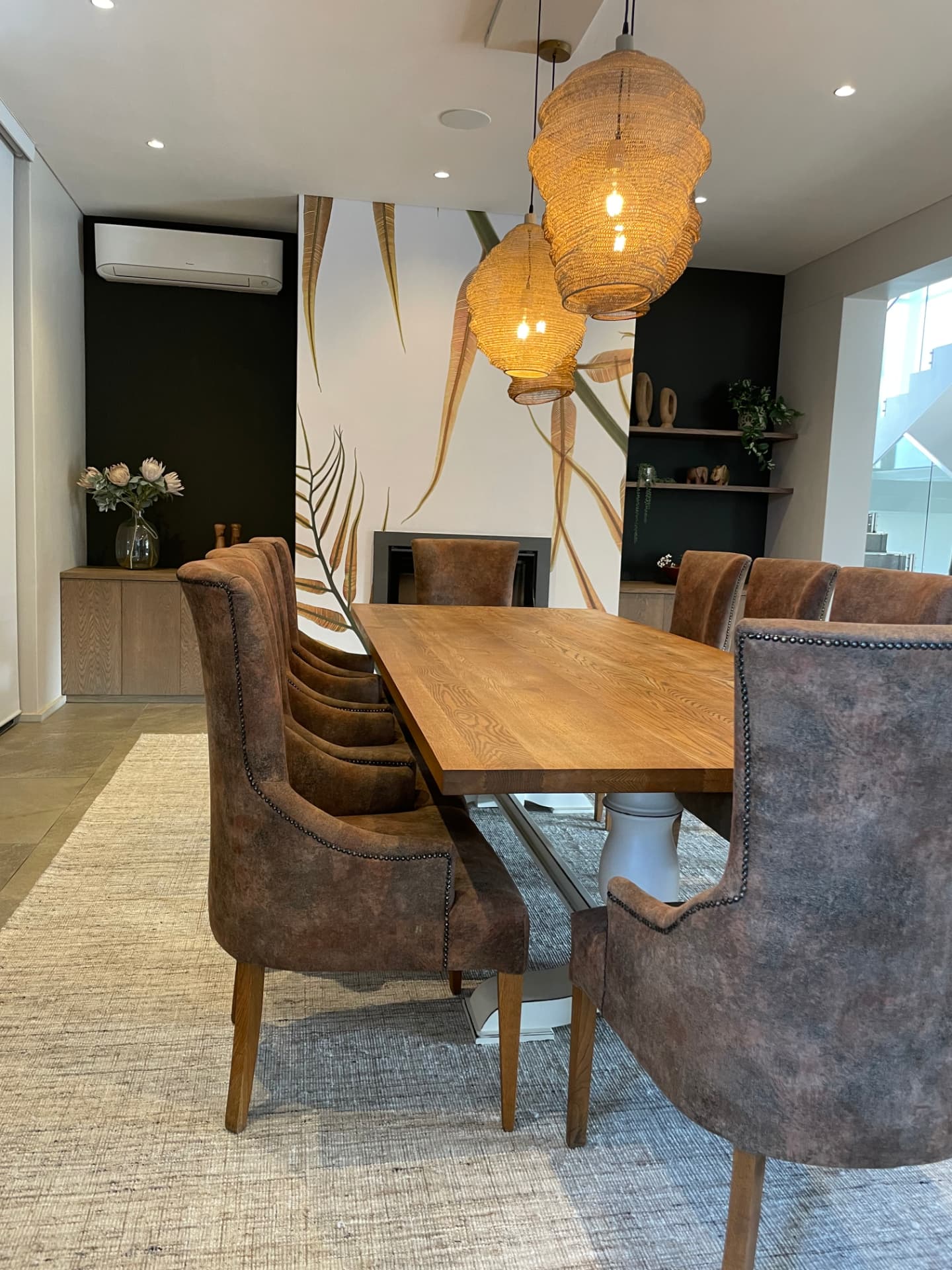 Dining room with botanical mural, woven pendants and leather wing chairs
