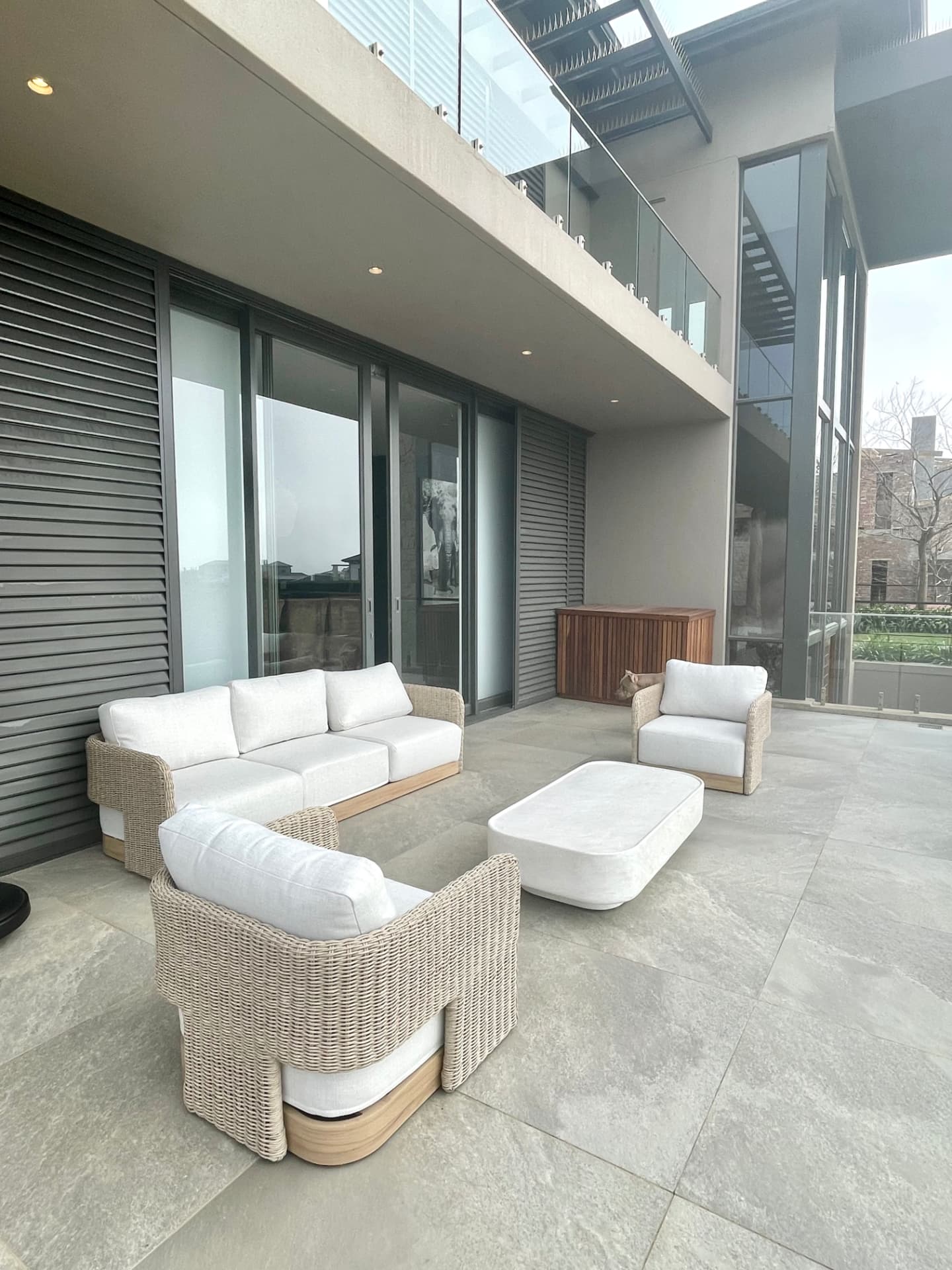 Covered terrace with woven outdoor lounge seating beneath a double-volume overhang