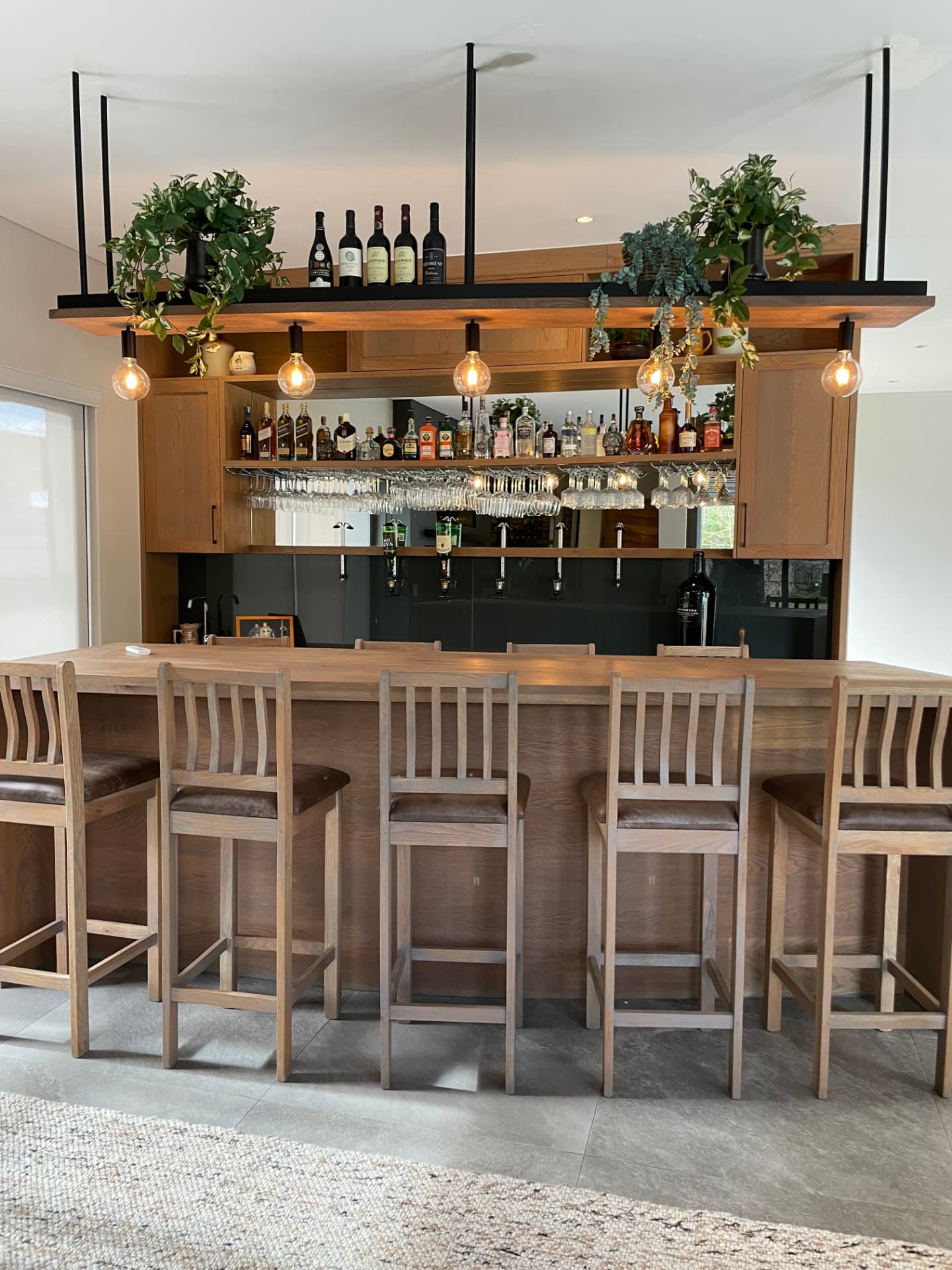 Bespoke oak bar with suspended shelving, pendant lighting and glass wine store