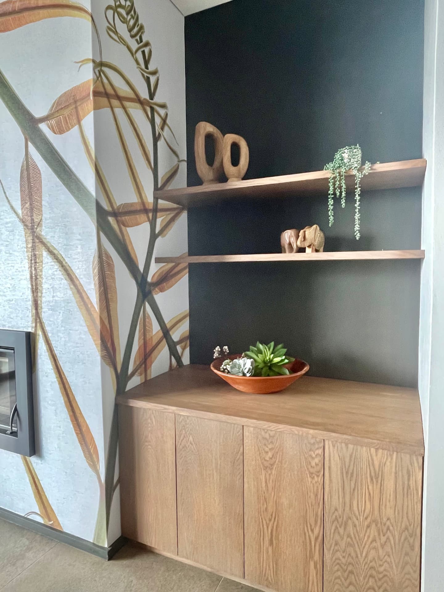 Corner oak cabinetry and shelving against a dark wall with mural detail
